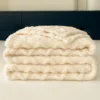 Folded beige fleece blanket with soft texture on a bed