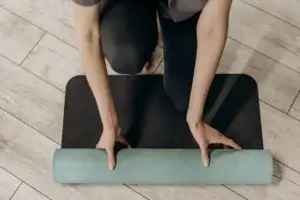 Person rolling out a yoga mat on wooden floor, preparing for a workout or meditation session